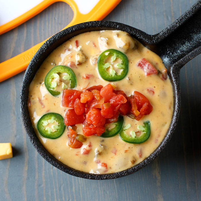 ['A close-up of a cast iron skillet filled with a cheesy dip topped with diced tomatoes and jalapeno slices.']