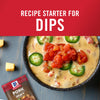 ['A bowl of cheesy dip with diced tomatoes and jalapenos, with a McCormick Pork Gravy packet in the foreground.']