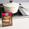 ['A package of McCormick Au Jus Gravy mix sits on a white countertop next to a white pot on a stovetop.']