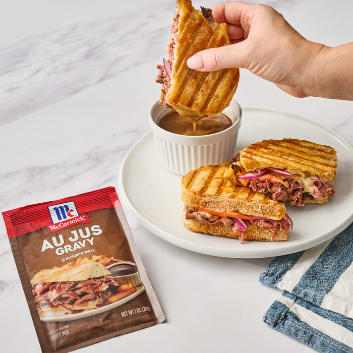 ['A hand dips a toasted sandwich into a bowl of McCormick Au Jus Gravy.']