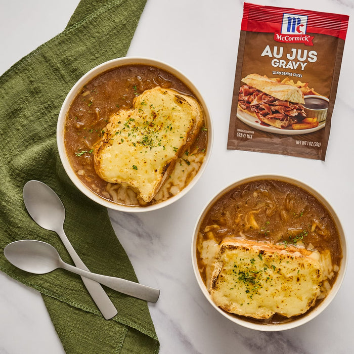 ['Two bowls of French onion soup with toasted bread topped with melted cheese and a packet of McCormick Au Jus Gravy mix.']