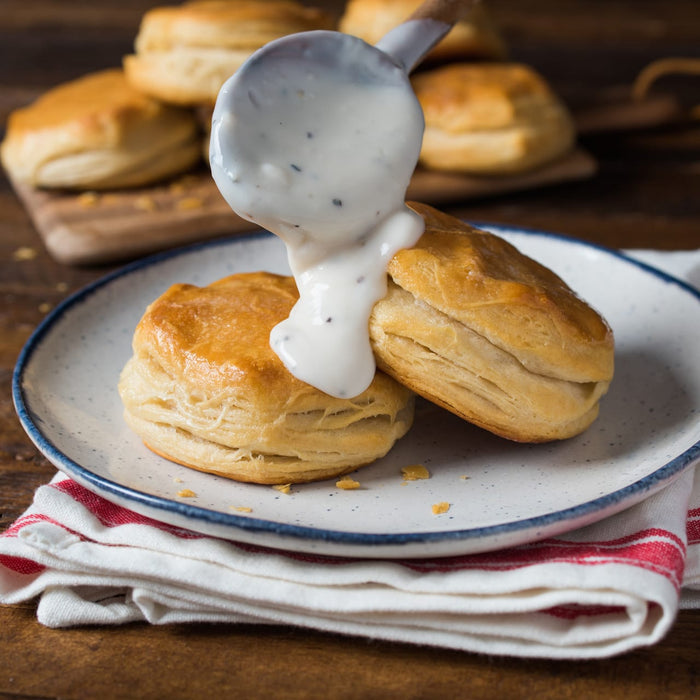 ['Two biscuits topped with white gravy on a plate with a red and white napkin.']