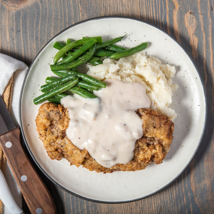 ['A plate of fried chicken with mashed potatoes, green beans, and gravy.']