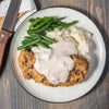 A plate of fried chicken with mashed potatoes green beans and gravy.