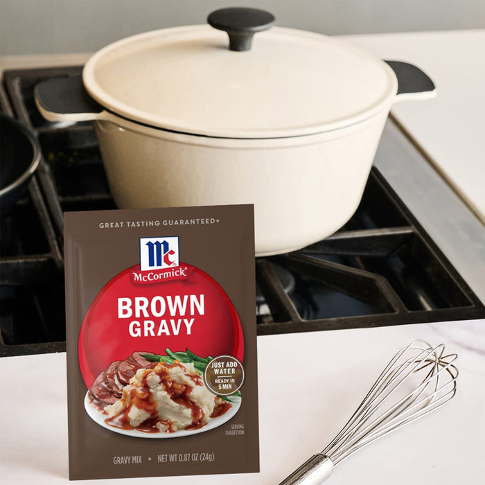 A package of McCormick Brown Gravy mix sits on a counter next to a whisk and a white pot on a stove.