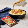 A bowl of mashed potatoes with McCormick Brown Gravy being poured over it.
