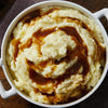 A bowl of mashed potatoes with gravy on top.