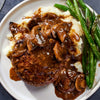 A plate of mashed potatoes a hamburger patty covered in gravy and green beans.