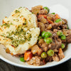 A white bowl filled with a hearty stew topped with mashed potatoes and parsley.