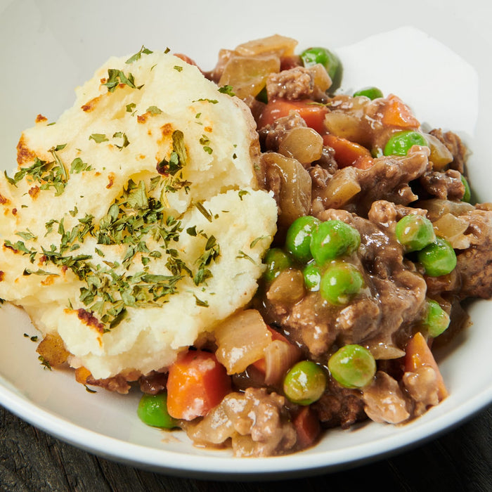 A white bowl filled with a hearty stew topped with mashed potatoes and parsley.