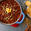 ['A close-up of a pot of baked beans with cheddar cheese, green onions, and bacon.']