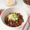 ['A bowl of chili topped with shredded cheese and green onions.']