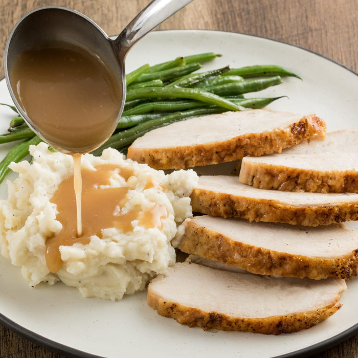 ['A plate of sliced turkey, mashed potatoes, and green beans with gravy being poured over the potatoes.']