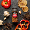 A bottle of McCormick's Roasted Garlic seasoning is surrounded by fresh ingredients like garlic, peppers, onions, and peppercorns.