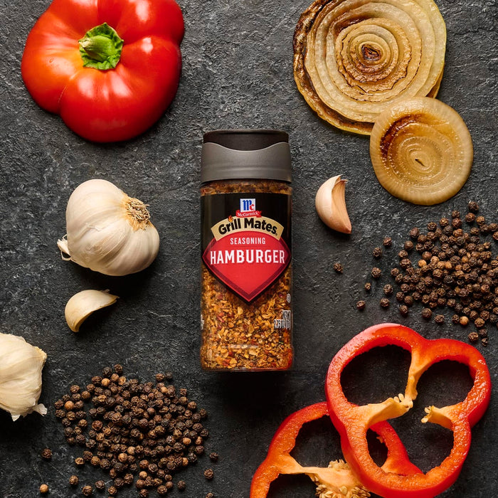 A bottle of McCormick's Roasted Garlic seasoning is surrounded by fresh ingredients like garlic, peppers, onions, and peppercorns.