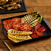 A black tray filled with grilled vegetables, including tomatoes, zucchini, squash, and red peppers, showcasing a healthy and colorful side dish.