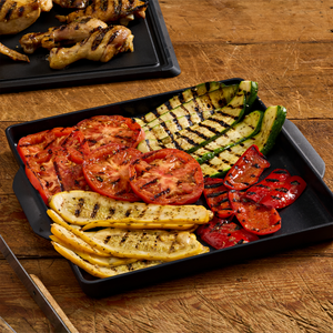 A black tray filled with grilled vegetables, including tomatoes, zucchini, squash, and red peppers, showcasing a healthy and colorful side dish.