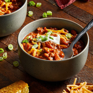 A bowl of chili topped with shredded cheese sour cream and green onions.
