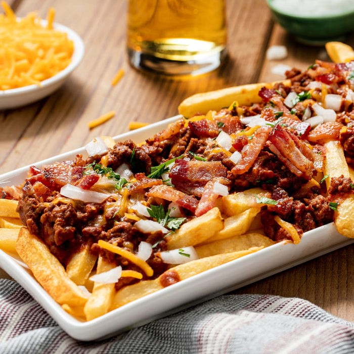 A plate of chili cheese fries topped with bacon and onions.
