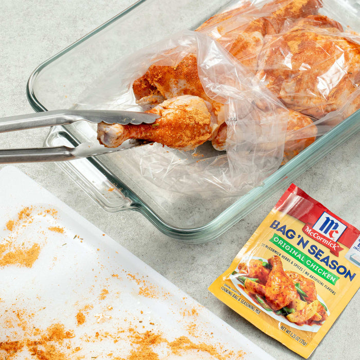 ["A close-up of a McCormick Bag'N Season Original Chicken package with a glass baking dish and tongs."]