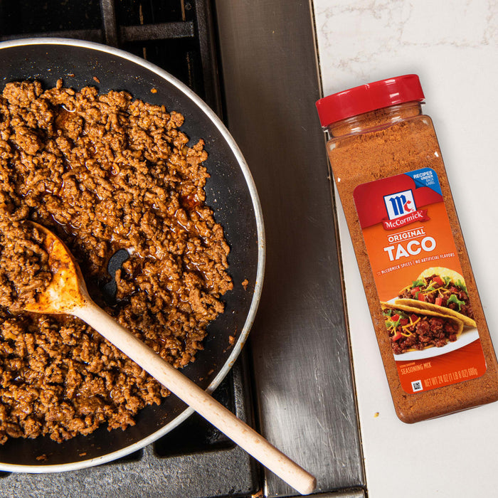 A close-up of a pan of ground beef with a wooden spoon and a jar of McCormick Original Taco Seasoning Mix.