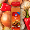 A jar of McCormick Original Taco Seasoning Mix with a red lid next to onions garlic and red peppers.