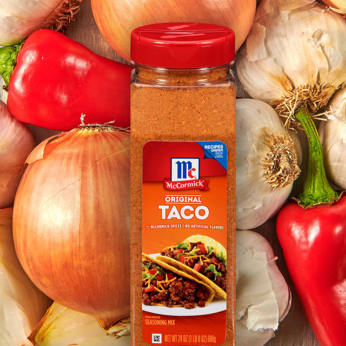 A jar of McCormick Original Taco Seasoning Mix with a red lid next to onions garlic and red peppers.