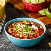 A bowl of chili with toppings of tortilla chips green onions and corn.