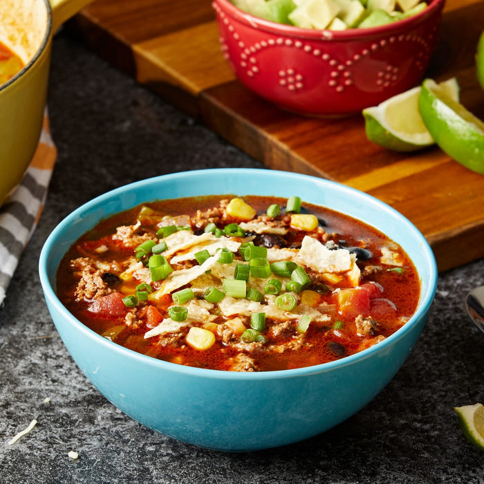 A bowl of chili with toppings of tortilla chips green onions and corn.