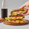 A stack of three quesadillas with ground beef lettuce tomato and sour cream on a wooden plate.