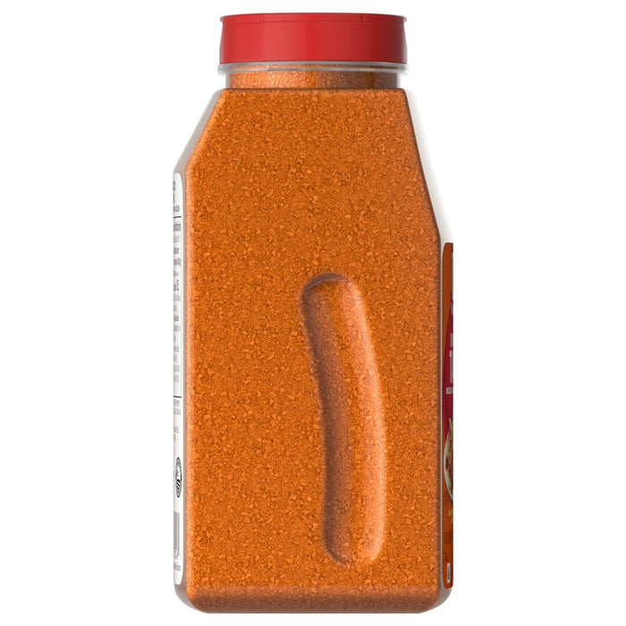 A side view of a large, clear container of Mccormick Taco Seasoning Mix 24 Oz, showing the orange-red granular spice and an indented grip.