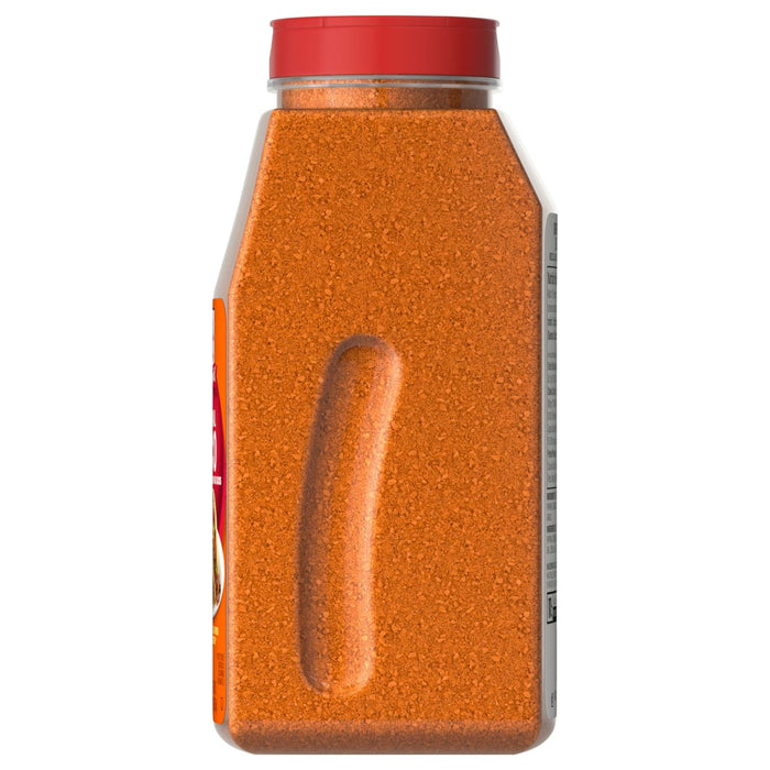 A side view of a large, clear container of Mccormick Taco Seasoning Mix 24 Oz, showing the reddish-orange granular spice and an indented hand grip.