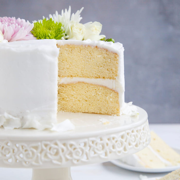 A white cake with white frosting and flowers on top is cut in half showing the layers of cake and frosting.