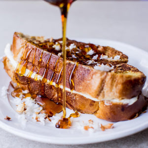 A stack of French toast with a creamy filling is being drizzled with syrup.