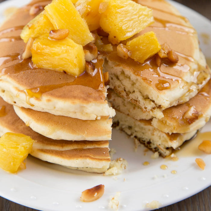 A stack of fluffy pancakes topped with pineapple chunks and syrup, showcasing a delicious breakfast option.