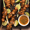 Grilled chicken skewers with lime wedges and dipping sauce are arranged on a grill pan, showcasing a flavorful and appetizing meal.