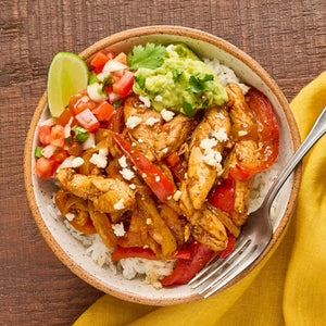 A vibrant bowl of chicken fajitas with rice, salsa, guacamole, and a lime wedge is shown from an overhead perspective.