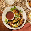 A plate of delicious-looking tacos with a side of dipping sauce and lime wedges.