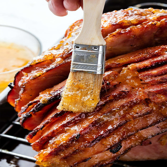 A glazed ham is being brushed with a sweet sauce, ready for serving.