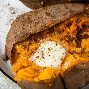 A baked sweet potato is split open and topped with a pat of butter and spices.