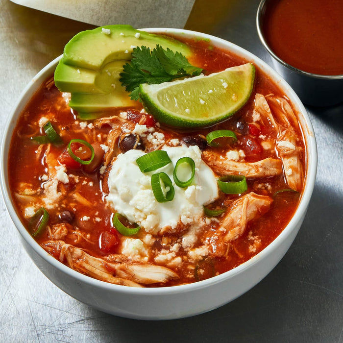 A bowl of hearty chicken tortilla soup is topped with avocado, lime, sour cream, and green onions.