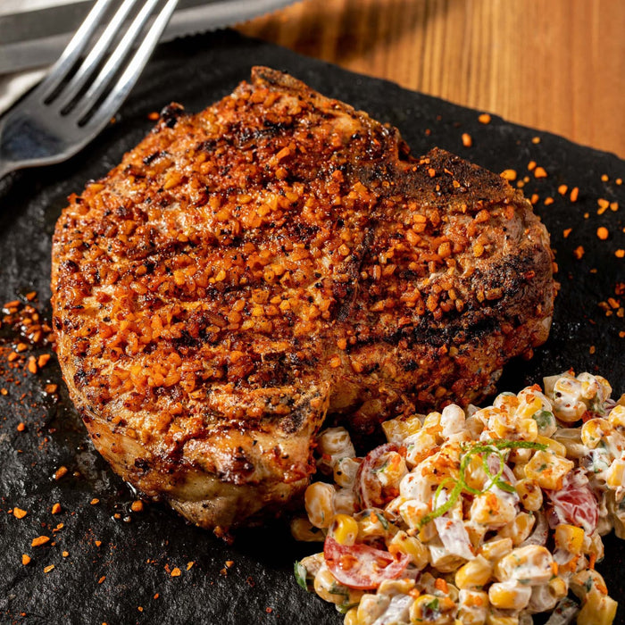 A grilled pork chop with a spicy crust is served alongside a colorful corn salad.