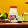 A bottle of McCormick Mayonesa with limes and salt on a wooden table.