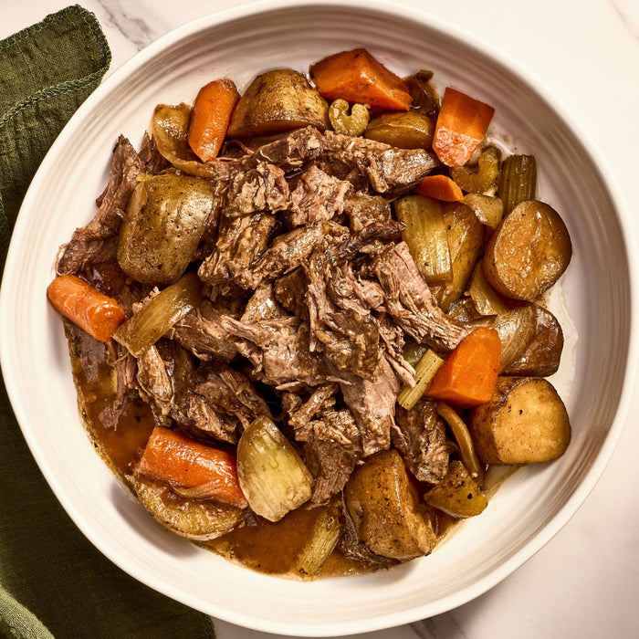 A white bowl filled with a hearty pot roast with potatoes, carrots, and onions.