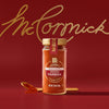 A glass jar of Mccormick Gourmet Smoked Paprika Organic 1.62 Oz sits on a red surface with a golden spoon holding some of the red spice, against a red background with the gold McCormick script logo.