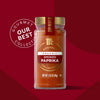 A jar of Mccormick Gourmet Smoked Paprika Organic 1.62 Oz, part of the Our Best Collection, stands against a red background.