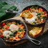 Two individual cast iron skillets present a savory breakfast of baked eggs, chickpeas, spinach, tomatoes, and feta, a perfect meal to incorporate Mccormick Gourmet Smoked Paprika Organic 1.62 Oz for added flavor.