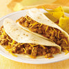Two soft tacos filled with ground beef cheese and a creamy sauce are on a white plate with tortilla chips.