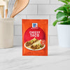 A packet of McCormick Cheesy Taco seasoning mix is displayed on a white marble surface.