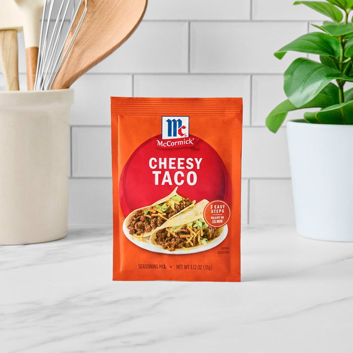 A packet of McCormick Cheesy Taco seasoning mix is displayed on a white marble surface.